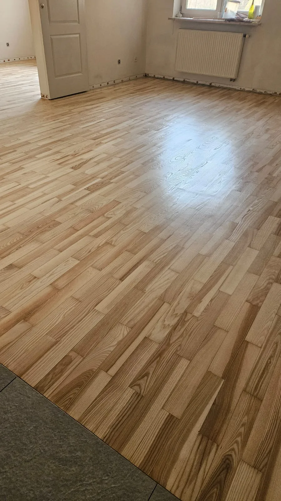Układanie parkietu na nowej podłodze, w tle widoczne drzwi i narzędzia