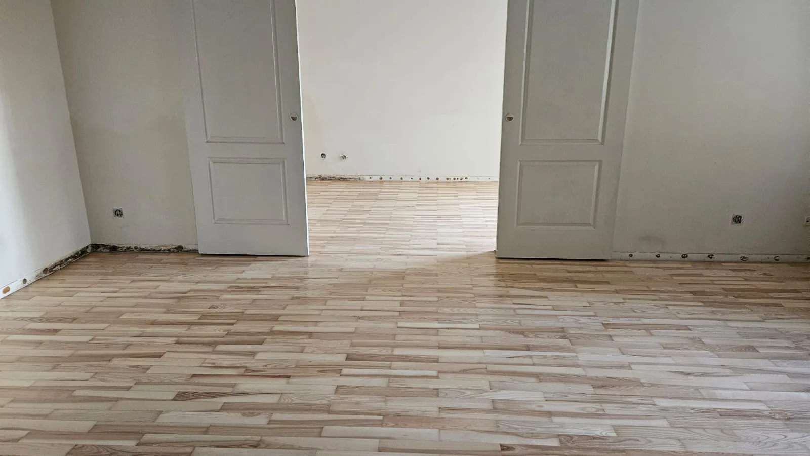 Wykończona podłoga z ułożonymi panelami w pomieszczeniu z dwiema białymi drzwiami